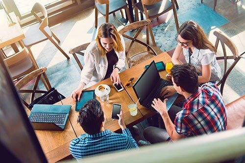 A photo of 4 students around a table using their gadgets